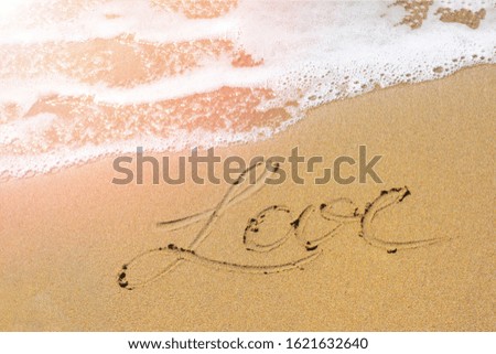 Yellow sand on Mediterranean sea shore with foamy wave and written word "love". Top view of handwriting letters.