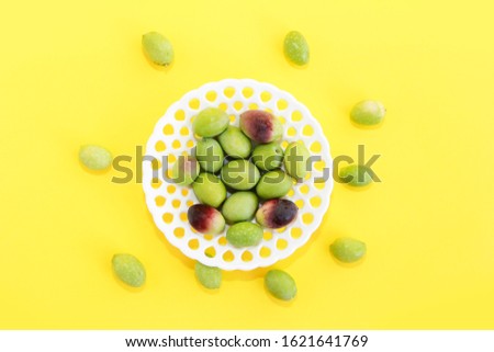 natural fresh green and burgundy olives in a white decorative plate on yellow background