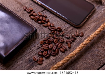 Still life photography of brown leather wallet, coffee beans, mobil phone and rope on vintage wooden background. Men casual concept, vintage and retro style.