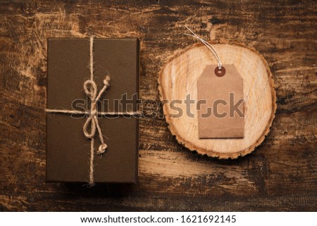 Brown gift box with burlap ribbon and tag card for inscription on old wooden table. Top view