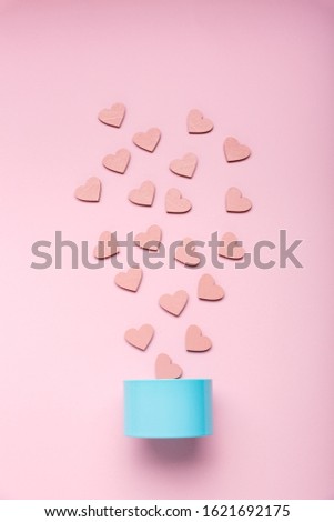 Blue little metal gift box and pink decorative hearts that fall out of it on a pink background. Top view