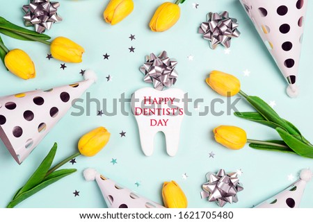 Dentist's Day greeting background with tooth, holiday caps and yellow tulips on a blue background. Happy Dentist's Day concept .