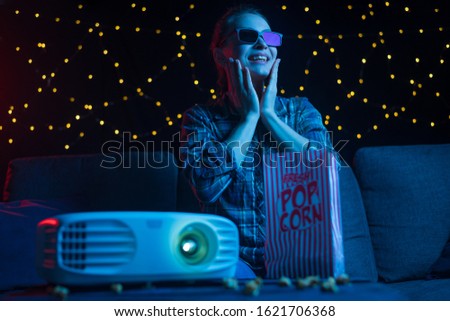 Home cinema at home, a girl watches films and movies on a projector with 3D glasses and popcorn