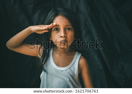 A little Asian girl in a pose shows an expression. Portrait of a child with a dark background. Cinematic look picture. Gestures education concept.