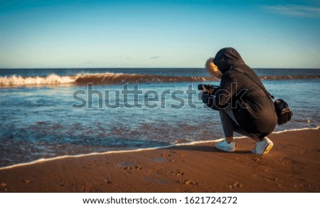 Woman taking photos of waves on her camera at the beach