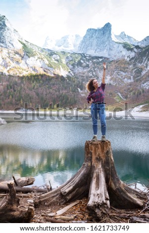 beautiful girl sits on a stump on a background of a mountain lake
