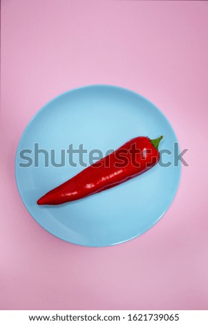 Red pepper on a blue plate on a pink background. Red hot chili pepper. Sweet delicious red pepper on isolated background