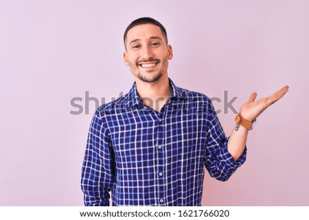 Young handsome man standing over isolated background smiling cheerful presenting and pointing with palm of hand looking at the camera.