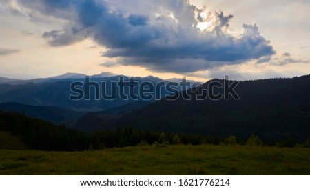 Majestic sunset and beautiful landscape in the mountains. Flooding fog between the peaks. Fragment of a blue sky with clouds. Summer beautiful sunny evening. Moving and red sun colorful sky background