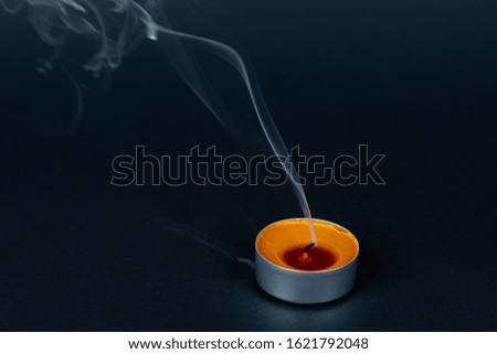 Extinct scented candle in a metal case on a black background with smoke.