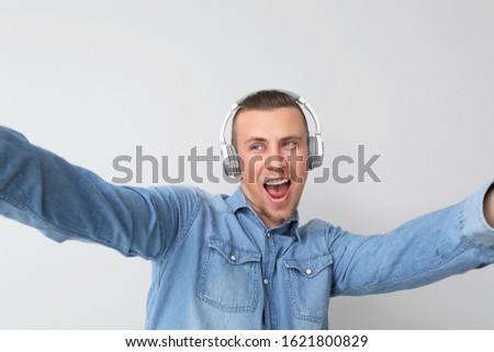 Handsome young man with headphones taking selfie on light background