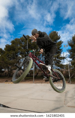 Conceptual extreme sports stills with out of focus parts. Dynamic vertical bmx shot of young white rider focused training making a barspin trick on a skatepark free of brands and cloudy sky background
