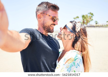 Young beautiful couple on vacation smiling happy and confident. Standing with smile on face hugging and making selfie by camera at the beach