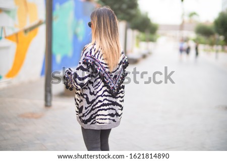 Young beautiful girl wearing sunglasses walking at the town street, standing on backview