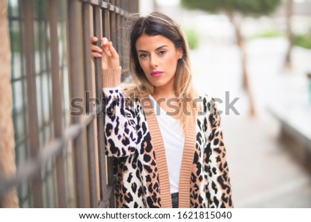 Young beautiful girl wearing animal print cardigan leaning on the wall at the town street