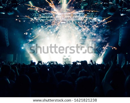 Multi coloured concert crowd inside a venue during a live band show performance on stage.