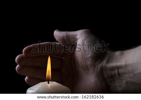 adult male hand protect burning candle, black background