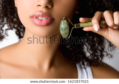 cropped view of african american girl using stone facial roller, isolated on grey Royalty-Free Stock Photo #1621837021