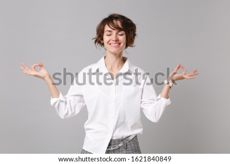 Smiling business woman in white shirt isolated on grey background. Achievement career wealth business concept. Mock up copy space. Hold hands in yoga gesture, relaxing meditating, keeping eyes closed