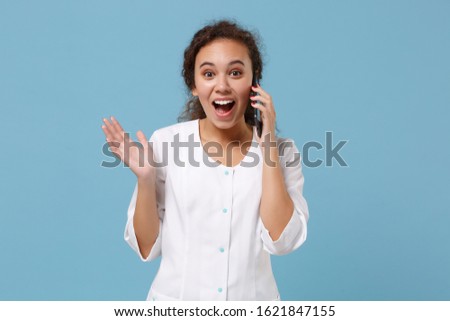 Excited african american doctor woman isolated on blue wall background. Female doctor in white medical gown talking on mobile phone. Healthcare personnel health medicine concept. Mock up copy space