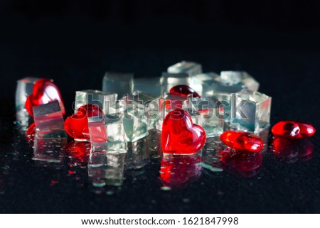 Holiday card for Valentine's Day. Ice cubes and red hearts on a black background.