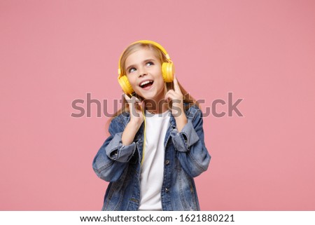 Charming little kid girl 12-13 years old in denim jacket isolated on pastel pink background children studio portrait. Childhood lifestyle concept. Mock up copy space. Listen music with headphones