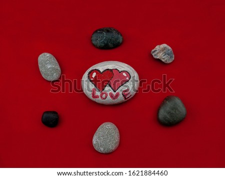 Painted stone with hearts on a red background among ordinary stones, for Valentine's Day