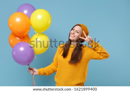 Smiling young woman in sweater hat posing isolated on blue background. Birthday holiday party people emotions concept. Mock up copy space. Celebrating hold colorful air balloons showing victory sign