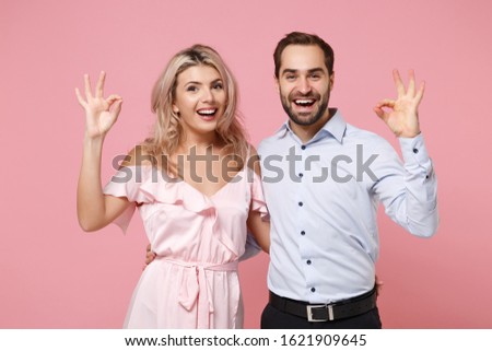 Funny young couple two guy girl in party outfit celebrating posing isolated on pastel pink background. People lifestyle Valentine's Day Women's Day birthday holiday concept. Showing ok okay gesture