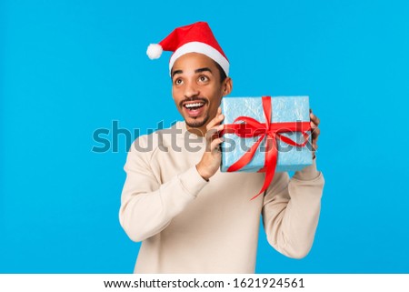 Secret santa left present under christmas tree man trying guess whats inside by shaking it. Cute and happy african-american guy holding cute box of gift and smiling, celebrating winter holidays