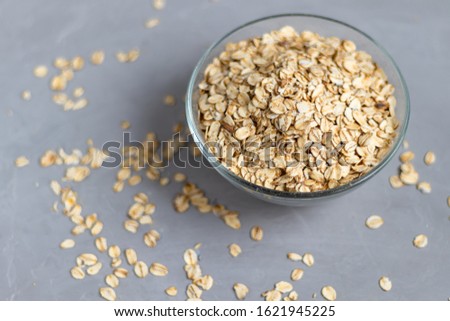 Raw oatmeal in a transparent bowl, prepared for brewing porridge. Healthy food, on a gray background.