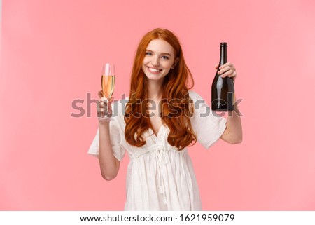 Cheers, congratulations my friend. Tender and happy, friendly-looking charming redhead woman in white dress, raising glass and holding champagne bottle, celebrating success, pink background