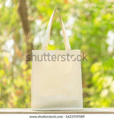 White cotton bag put on wooden table with space for text or advertising. Cotton bag can use for shopping to replace plastic bag on green nature background