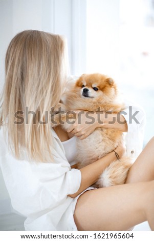 A beautiful young blond woman sits on the floor with her dog, hugs her. Dog breed Pomeranian