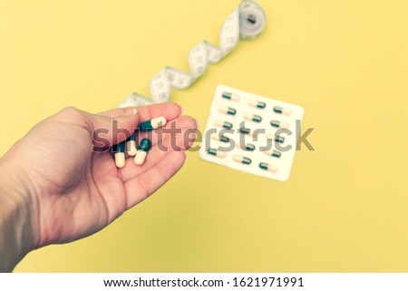 Diet pills in woman's hand and measuring meter on yellow background. Losing weight concept.
