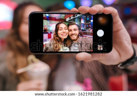 Image of a happy cheery optimistic young loving couple sit in retro bright cafe take a selfie by mobile phone indoors.