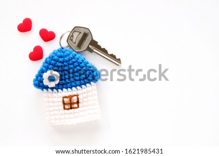 Mini blue roof crocheted house with key and three red hearts on white background, shot from top view. Concept for family, house insurance, financial home loan or money saving for house buying