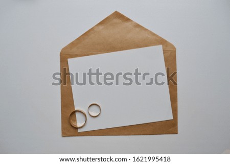 Artistic mockup for your artwork with craft paper envelope, wedding rings and empty card shot from the top. Wedding invitation. Flat lay minimalistic composition.