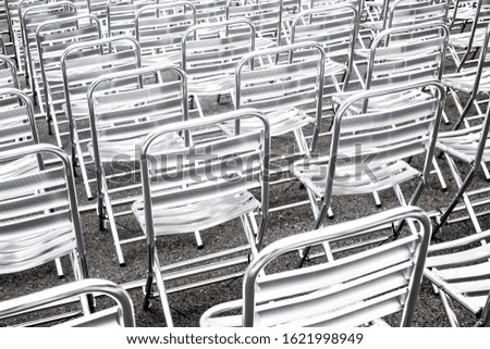 Shiny metallic chairs in rows prepared for public event. Empty seats in public space.Abstract urban background. Rhythms and perspective, high contrast image.