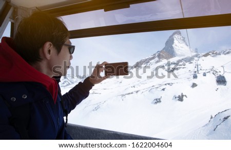  Tourist man which he is a  hands holding take a picture by smartphone view of Gornergrat, Zermatt, Matterhorn ski resort in Switzerland with cable chairlift transport