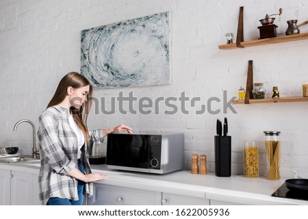 side view of smiling woman looking at microwave in kitchen