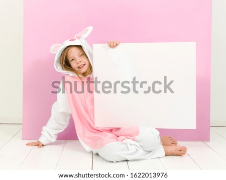 pretty blonde girl with cozy rabbit costume and white sign is posing in the studio and is happy