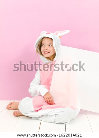 pretty blonde girl with cozy rabbit costume and white sign is posing in the studio and is happy