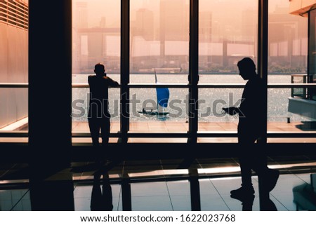 business people looking on mobile phone inside office building with ocean view window and sailing boat -