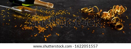 Golden confetti with streamers and champagne on noble black surface. Glamourös background for celebrations and holidays with space for text and design.