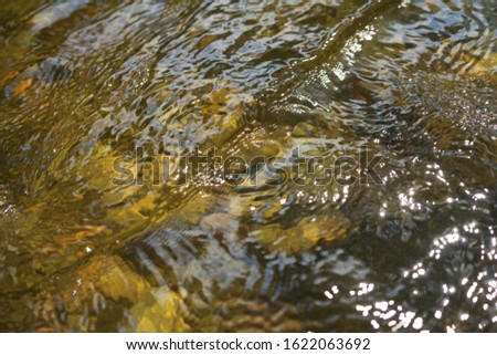 Stone beneath serene river water, river water waves brushing through the stones.