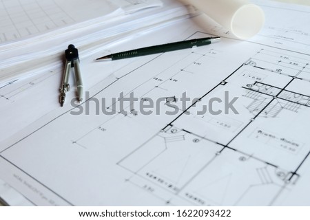 Selective focus of pencil, other drawing instruments with blurred Architectural drawing blueprint with blueprint roll and on the worktable as a background. Draft of project and sketching before build.