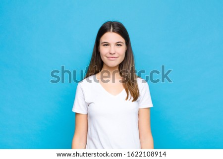 young pretty woman smiling positively and confidently, looking satisfied, friendly and happy against blue wall