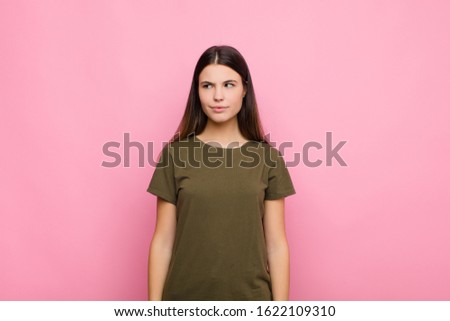 young pretty woman wondering, thinking happy thoughts and ideas, daydreaming, looking to copy space on side against pink wall