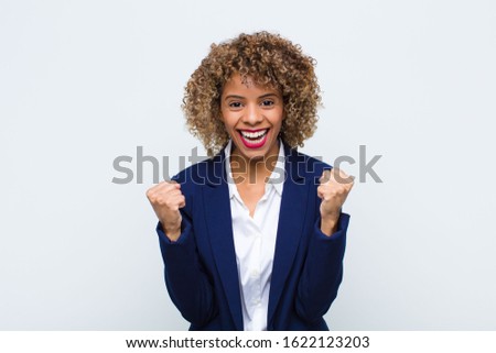 young woman african american feeling shocked, excited and happy, laughing and celebrating success, saying wow! against flat wall